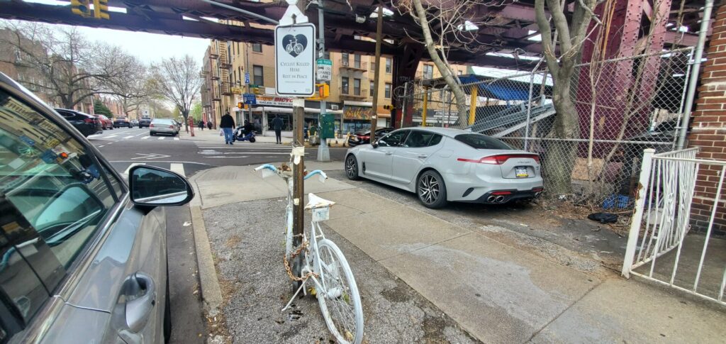 White ghost bike attached to sign post below an X and a "Cyclist Killed Here Rest in Peace" sign on 25 Street at 23 Avenue in Astoria, Queens.